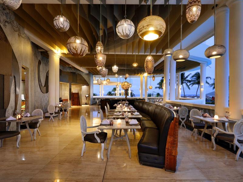 Restaurante elegante con mesas y sillas junto a grandes ventanas y lámparas colgantes doradas.