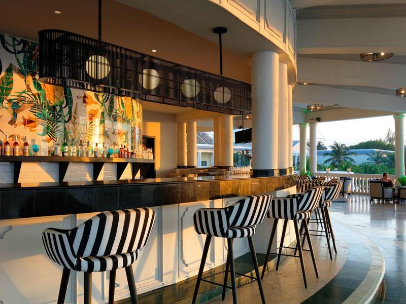 Moderner Hotelbarbereich mit schwarz-weiß gestreiften Barhockern und tropischer Wanddekoration.