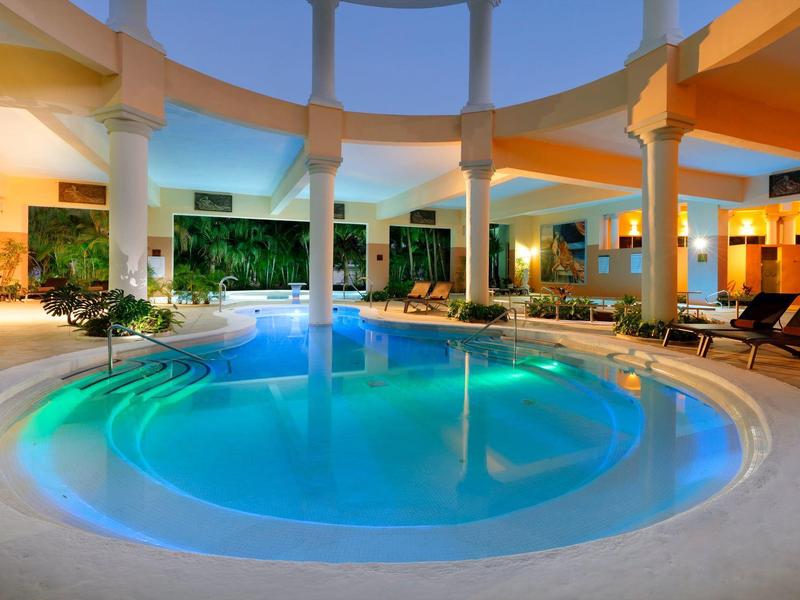 Beleuchteter Innenpool in einem modernen Hotel mit Säulen und Liegestühlen.