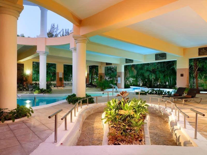 Überdachter Außenbereich mit Schwimmbecken, Säulen und grünen Pflanzen in der Mitte.