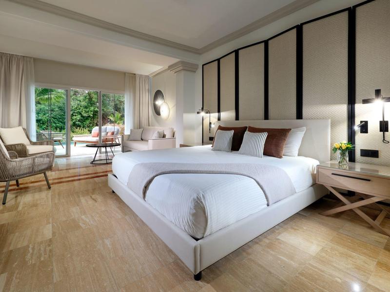 Modernes Schlafzimmer mit großem Bett, Holzfußboden, Sitzstuhl und Terrasse mit Gartenblick.