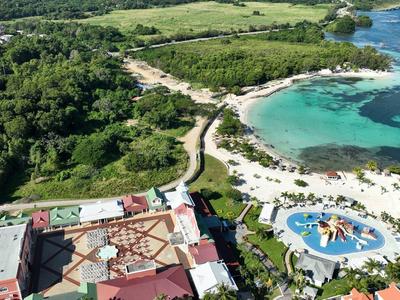 Luftaufnahme eines Küstenresorts mit Pool, Sandstrand und grün bewaldeter Umgebung.
