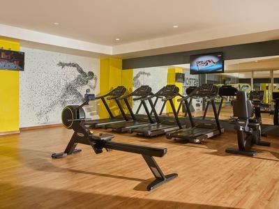 Moderner Fitnessraum mit Rudergerät, Laufbändern, gelben Wänden und Holzboden.