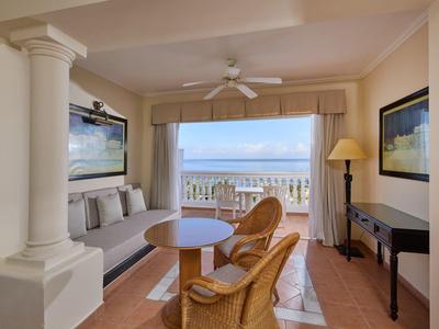 Helles Wohnzimmer mit Sitzbereich, Korbstühlen, Deckenventilator und Blick auf Meer durch großes Fenster.