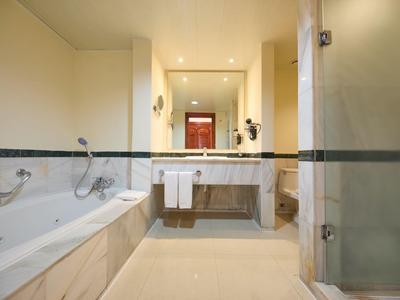 Helles Badezimmer mit Badewanne, großem Spiegel, Waschtisch und Dusche mit Glaswand.