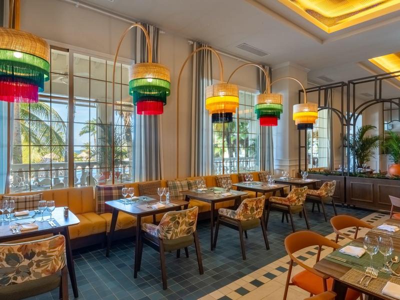 Světlá restaurace s barevnými lampami a výhledem na palmy přes velká okna.