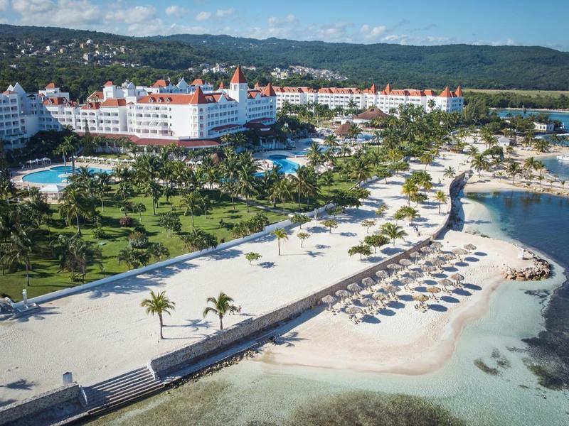 Velký hotel u pláže s bazény, palmami a lehátky u průzračného moře.