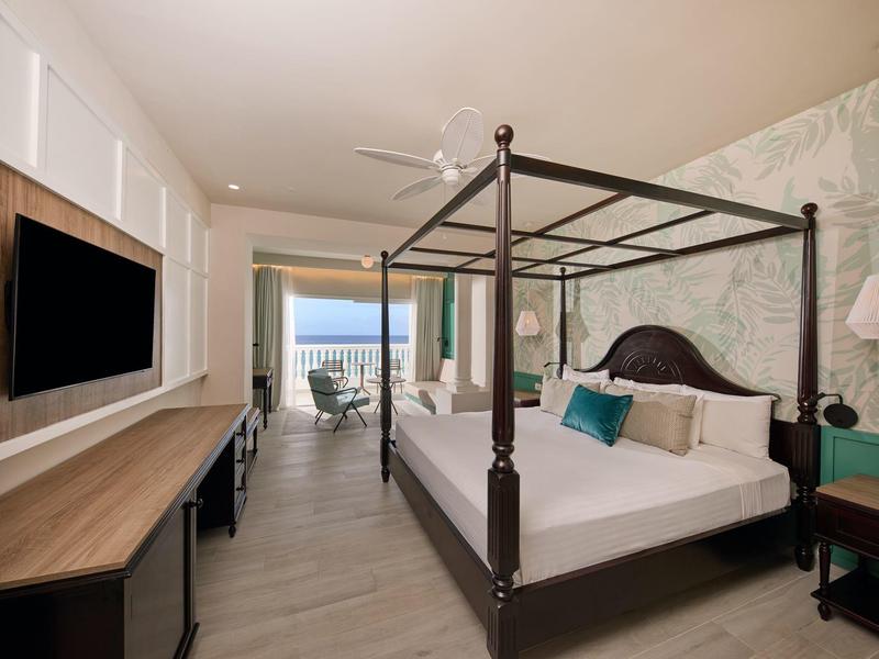Hotelový pokoj s postelí s nebesy, televizí, stolem a balkonem s výhledem na moře