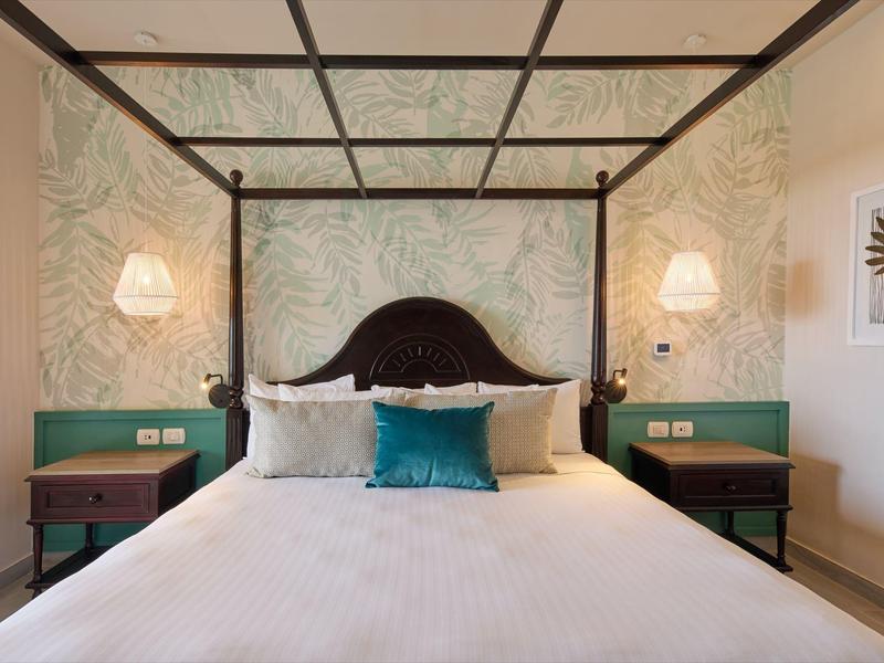 Moderní hotelový pokoj s postelí s baldachýnem, zelenými akcenty a dekorativní tapetou.