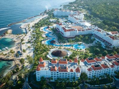 Großes Resort mit weißen Gebäuden, roten Dächern, vielen Pools und Palmen an der Küste.