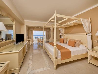 Helles Schlafzimmer mit Himmelbett, beige Wänden, Fernseher und Blick auf Terrasse mit Meerblick.