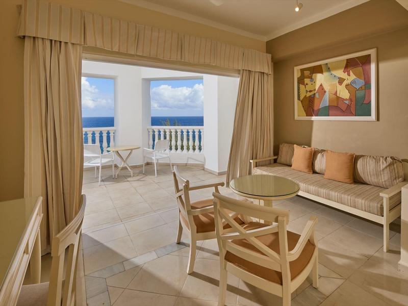 Elegant hotelkamer met balkon en zeezicht, gezellige zithoek en moderne inrichting.