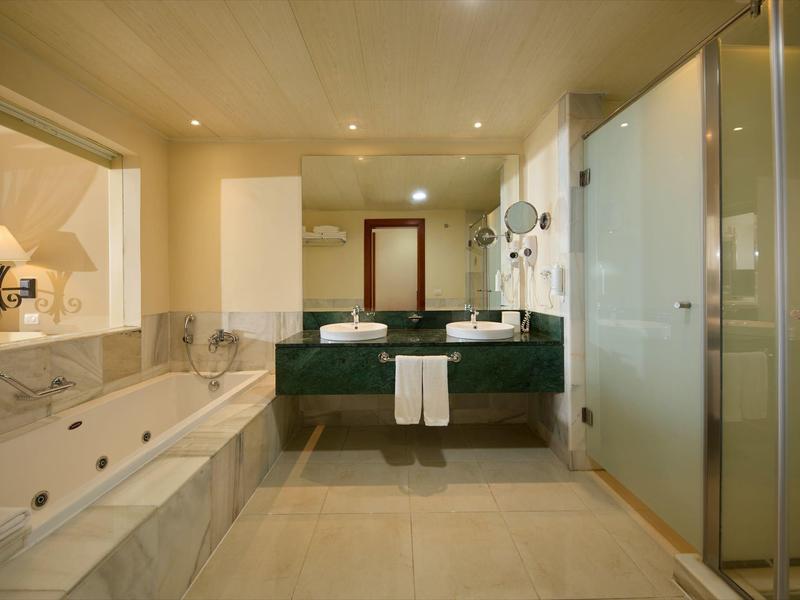 Moderne hotelbadkamer met groot bad en dubbele wastafels onder warm licht.