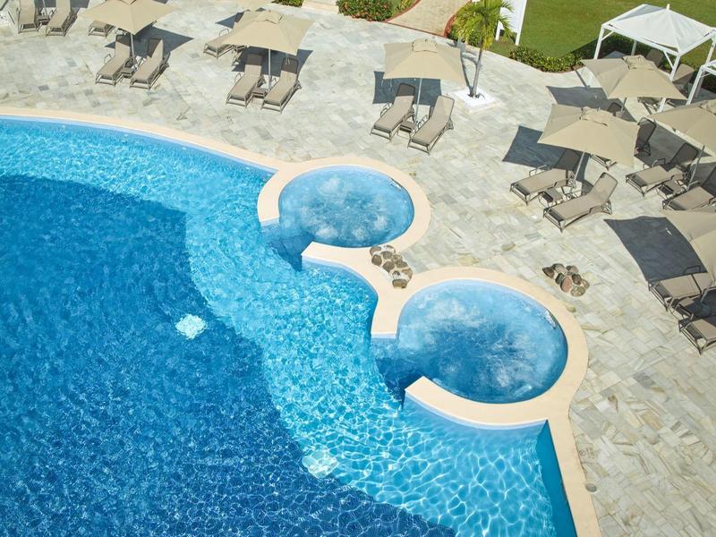 Blauw hotelzwembad met twee verbonden ronde whirlpools op stenen tegels omringd door parasols en ligstoelen.