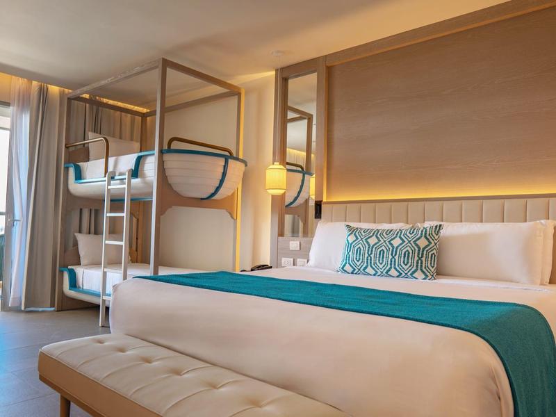 Modernes Hotelzimmer mit Doppelbett, Etagenbett, Sitzbereich, Holzrahmen und warmem Licht.