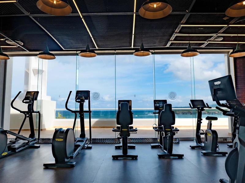 Modernes Fitnessstudio mit Sportgeräten, großem Fenster und Blick auf das Meer.