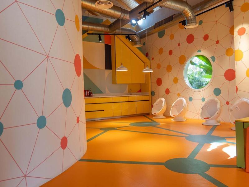 Bunter Spielraum mit orangen Boden, kreisförmigen Fenstern und bunten Punkten an Wänden.