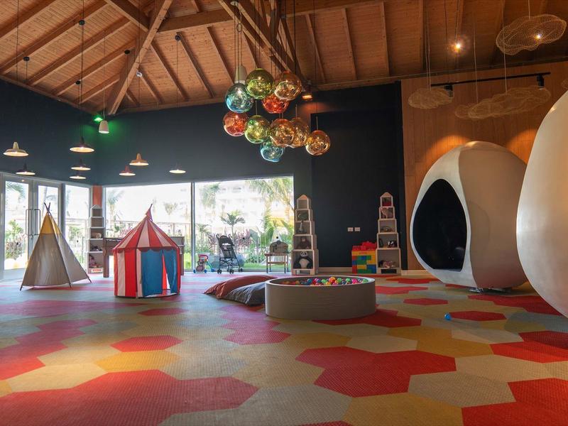 Großer Spielraum mit buntem Teppich, Holzdach, Hängesesseln und Zelt für Kinder.