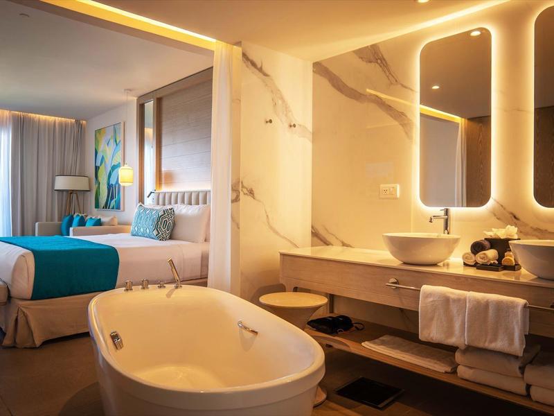 Modernes Hotelzimmer mit Badewanne, Doppelbett, großem Spiegel und Fenster mit Ausblick.