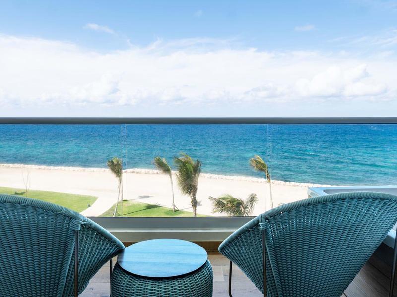 Blick vom Balkon mit zwei blauen Stühlen und Tisch aufs Meer, Strand und blaue Himmel mit Wolken.