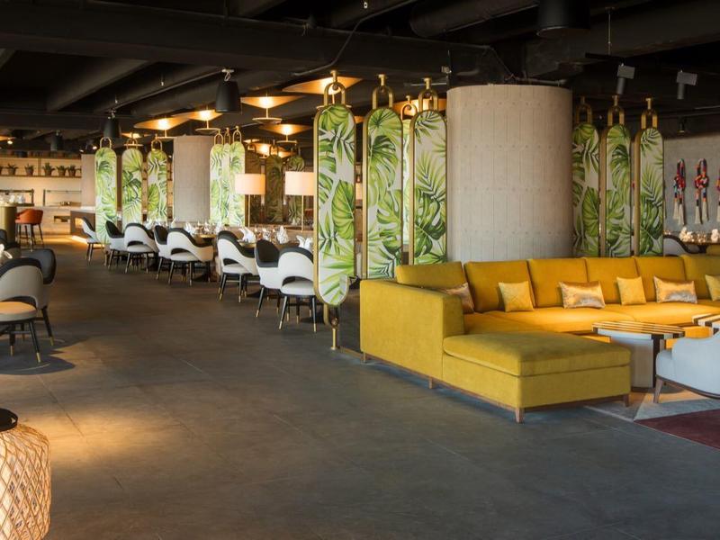 Weitläufige Lounge mit gelben Sofas, modernen Sesseln und warmem Licht in einem offenen Raum.