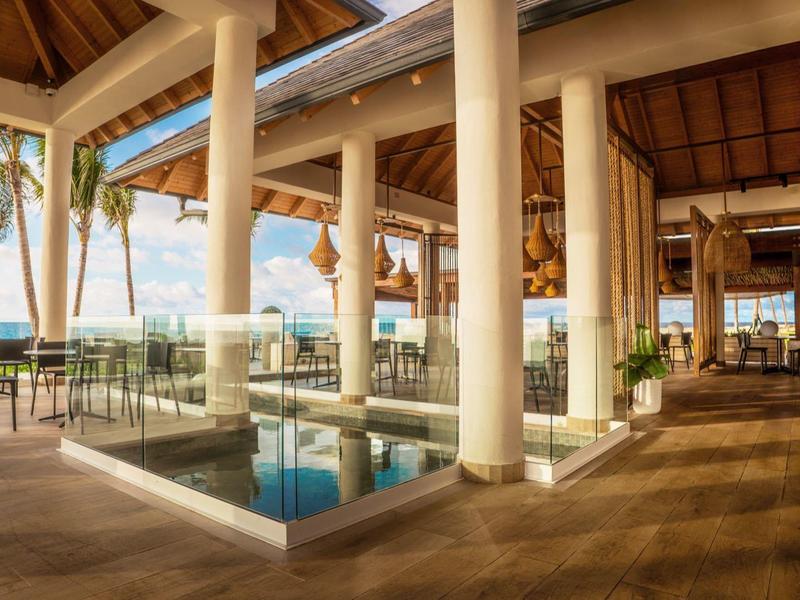 Offener Pavillon mit Säulen, Holzdecke und kleinem Wasserbecken, Blick aufs Meer und Palmen.