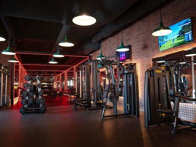 Moderner Fitnessraum mit roten Wänden, verschiedenen Kraftgeräten und schwarzen Bodenfliesen.