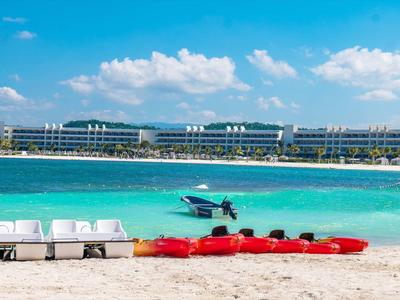 Beach with lounge chairs, kayaks, and view of modern hotel by turquoise sea.