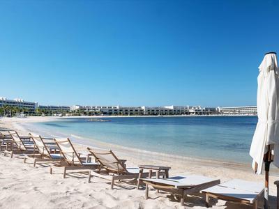 Breiter Sandstrand mit vielen Liegestühlen und blauem, klarem Himmel am ruhigen Meer.