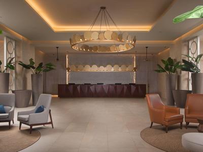 Modern luxury hotel lounge area with seating groups, plants, and elegant chandelier.