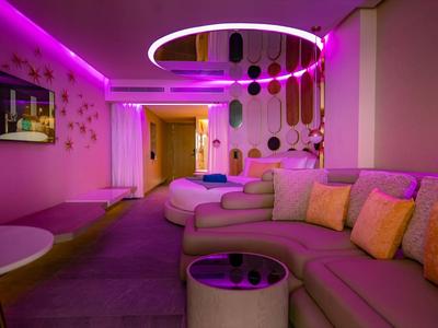 Modern hotel room with purple LED lighting, sofa, and hanging lamps.
