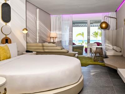 Modern hotel room with round bed, seating area, and balcony with a view.