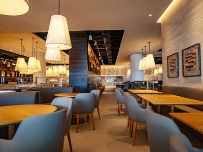 Modern hotel bar with cozy armchairs, wooden tables, and warm lighting.