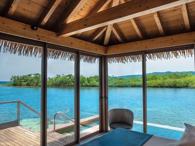 View from a wooden cabin with glass walls overlooking a turquoise lagoon and green islands.