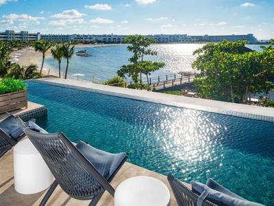 View of a pool with chairs by the water, palm trees, and cityscape in the background in sunlight.