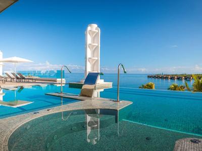 Luxurious pool area overlooking the sea with loungers and umbrellas under clear skies.