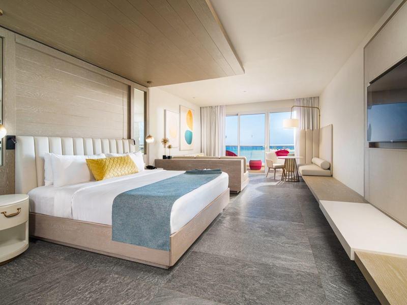 Modern hotel room with large bed, flat-screen TV, and window overlooking the sea.