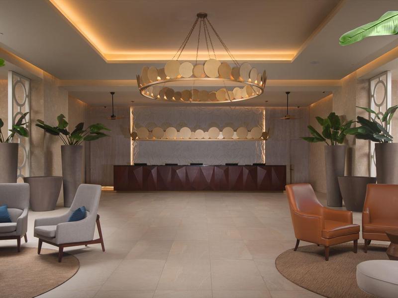 Modern luxury hotel lounge area with seating groups, plants, and elegant chandelier.