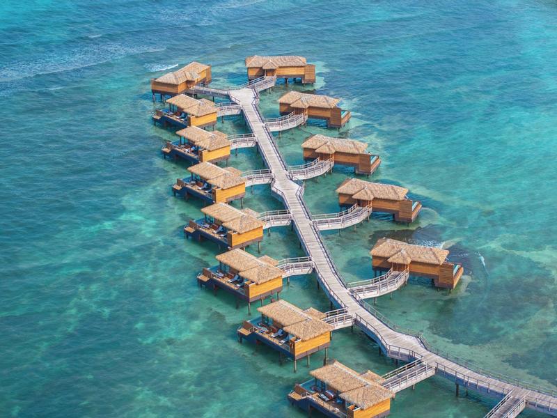 Overwater bungalows connected by walkways over clear turquoise water in a tropical resort