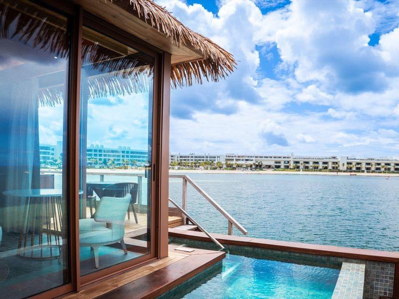 View of an overwater bungalow terrace with private pool and sea panorama under cloudy sky.