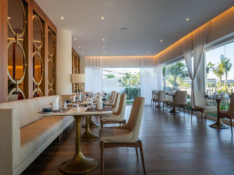 Modern hotel restaurant with stylish chairs, tables, large window, and view of palm trees.