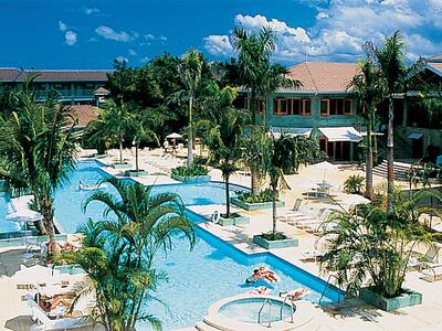 Hotelpoolbereich mit Liegestühlen, Palmen und blauem Himmel an einem sonnigen Tag.
