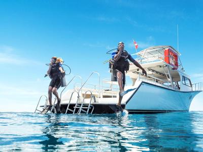 Zwei Taucher springen vom Boot ins klare blaue Meer unter einem wolkenlosen Himmel.