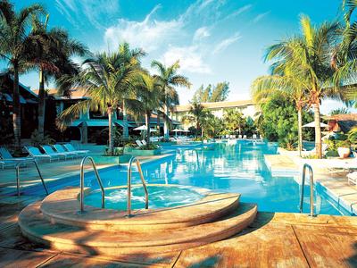 Hotelpool mit Treppen und Liegestühlen, umgeben von Palmen unter blauem Himmel.