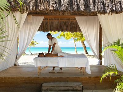 Person erhält Massage auf einer Liege in einer offenen Hütte am Strand mit Blick auf das Meer.