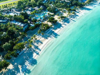 Widok z lotu ptaka na hotel przy białej piaszczystej plaży z turkusowym morzem i palmami.
