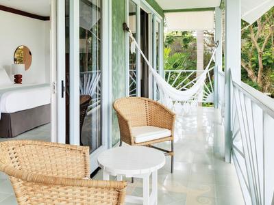 Balkon mit Korbstühlen, kleinem Tisch und Hängematte neben einem Hotelzimmer mit Gartenblick.