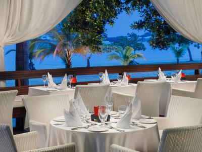 Elegant gedeckte Tische auf einer Terrasse mit Meerblick und Palmen bei Dämmerung.