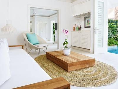 Helles modernes Wohnzimmer mit weißen Wänden, Holzsideboard, blauem Stuhl und direktem Poolzugang.