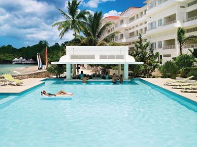 Großer Hotelpool mit Swim-up-Bar, umgeben von Liegestühlen und Palmen.